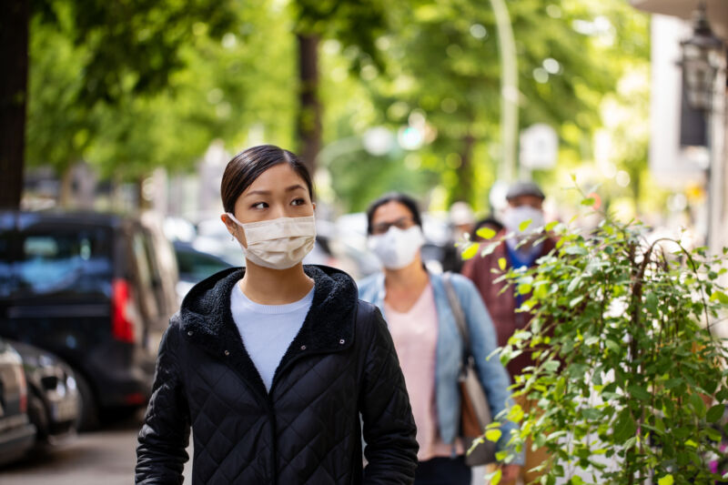 一个蒙面的女人沿着一个穿着前沿的城市街道走。