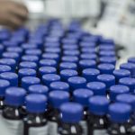 Tiny bottles with plastic lids crowd a conveyor belt.