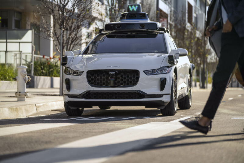 One of Waymo's sensor-studded Jaguar I-Paces observes a pedestrian crossing the road in front of it.