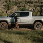 A man is about to open the door of a Rivian truck in the wilderness