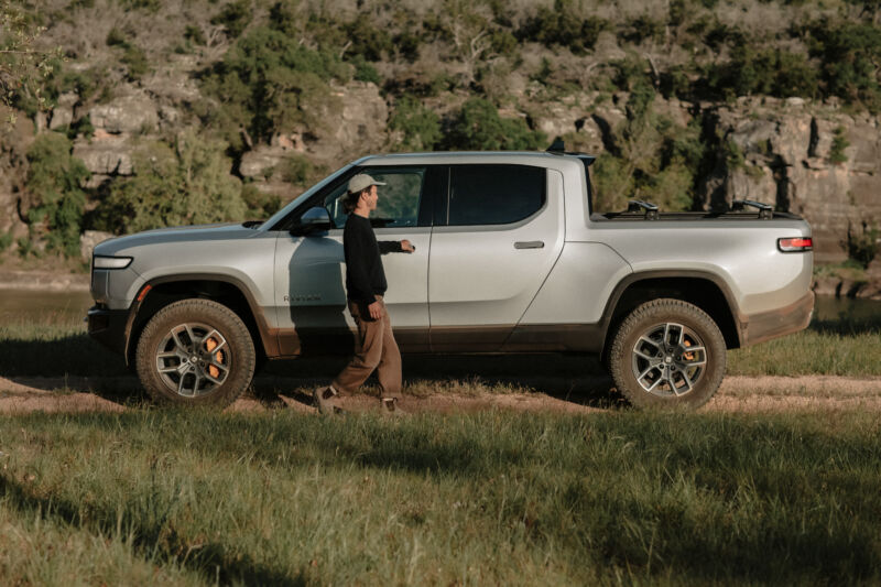 A man is about to open the door of a Rivian truck in the wilderness