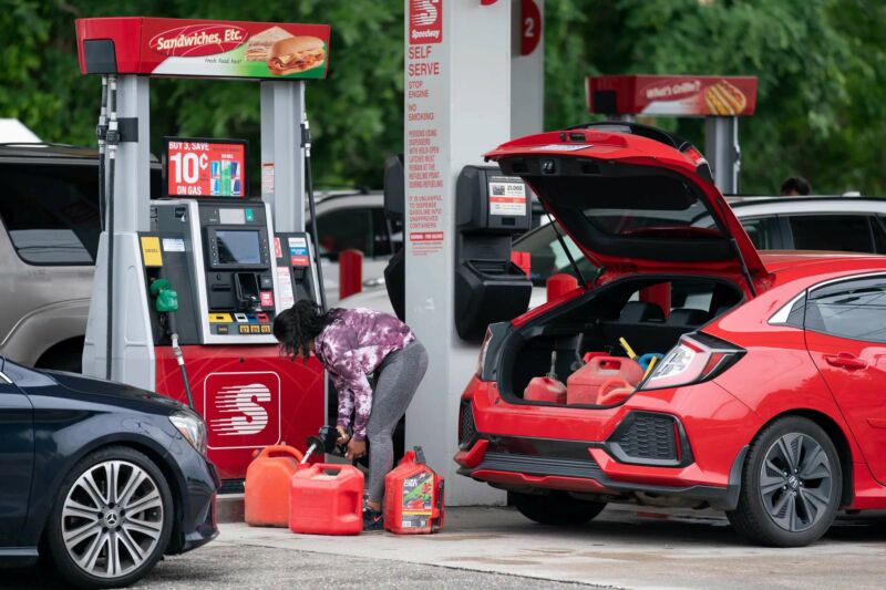 Une femme dans une station-service remplit plusieurs bonbonnes de gaz.