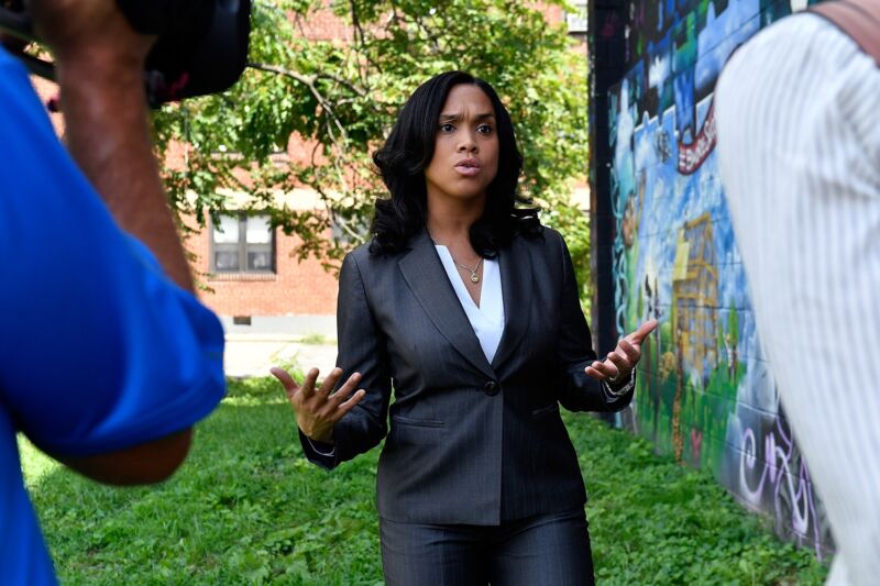 Baltimore chief prosecutor Marilyn Mosby standing outside and talking to a reporter as a person holding a camera films.