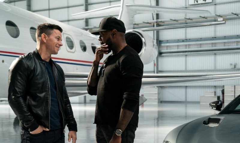 Two cool bros chat in a hangar in front of private jet.