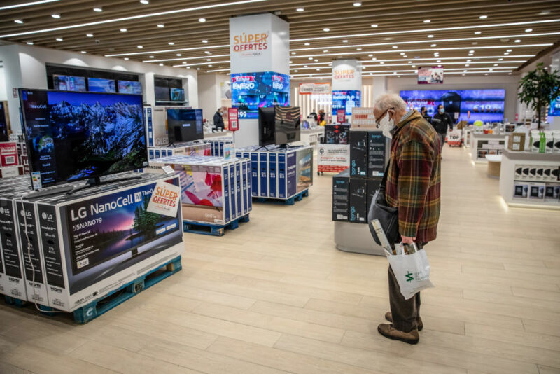 A masked shopper slumps as he watches a flat screen TV in a large box store.