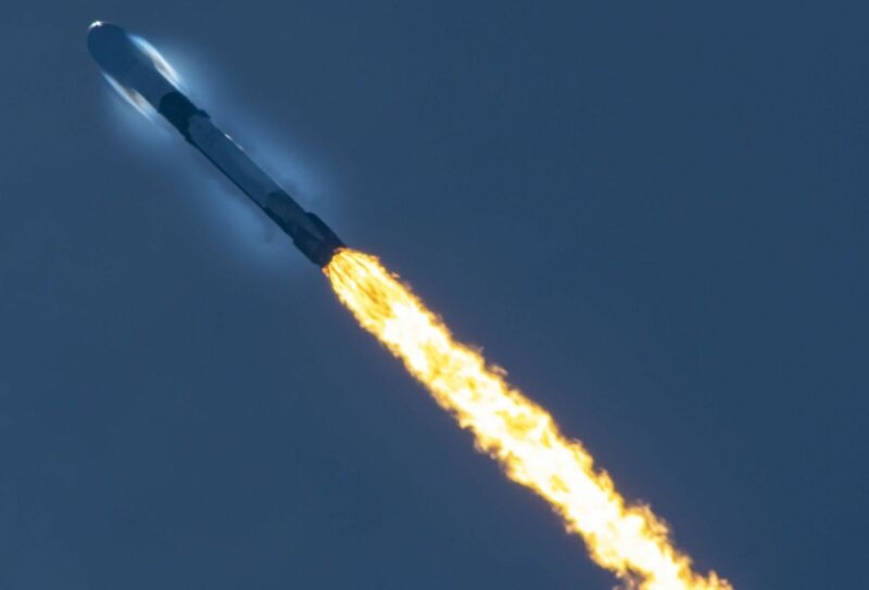 A launching rocket leaves a trail of flame against a dark blue sky.