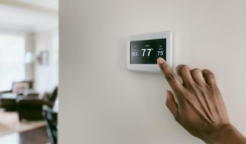 Close-up of woman’s hand adjusting air conditioning setting on thermostat.