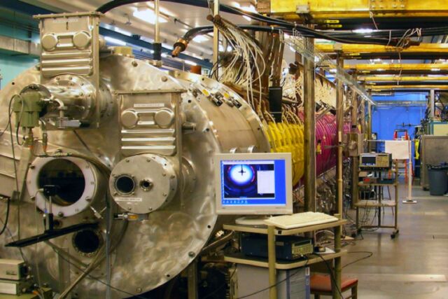 Panoramaansicht des großen Plasmageräts, einer zylindrischen Vakuumkammer von etwa 20 m Länge und 1 m Durchmesser, die in starke axiale Magnetfeldspulen (lila und gelb) gehüllt ist.