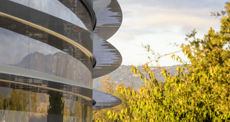 A tree-lined campus surrounds a glass and steel building with more floors.