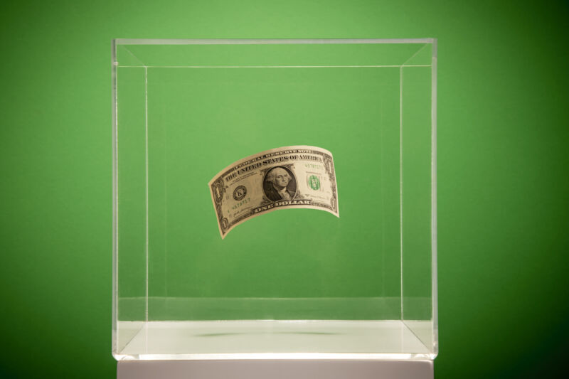 A dollar floats in a museum-style plastic display case.