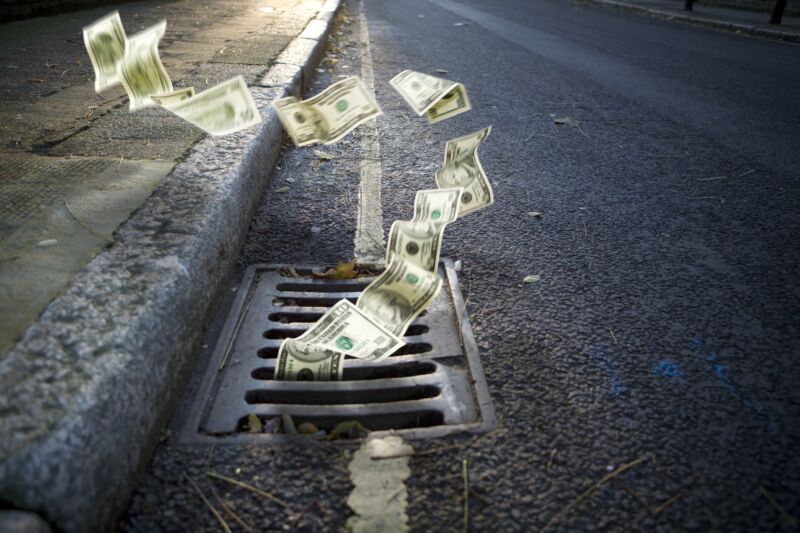 Money falling into a grate on the side of a street.