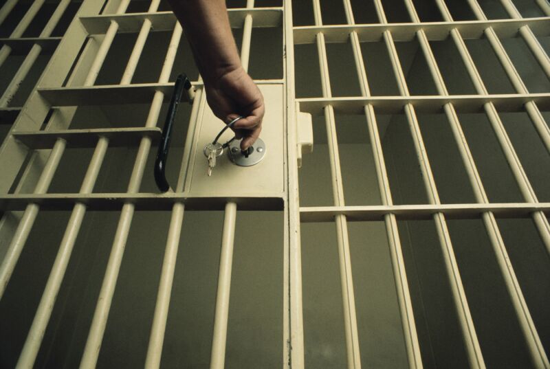 A person's hand inserting a key into the lock on a jail-cell door.