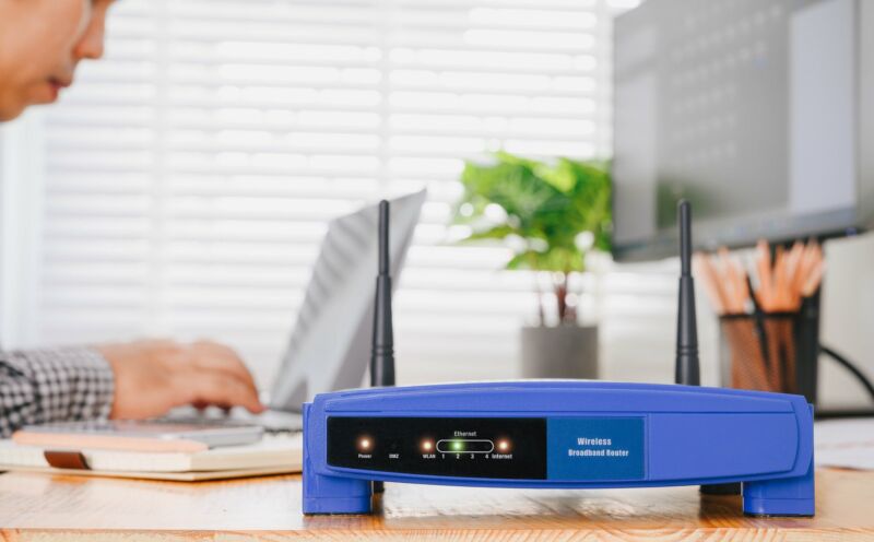 A wireless router on a desk in an office where a man is typing.