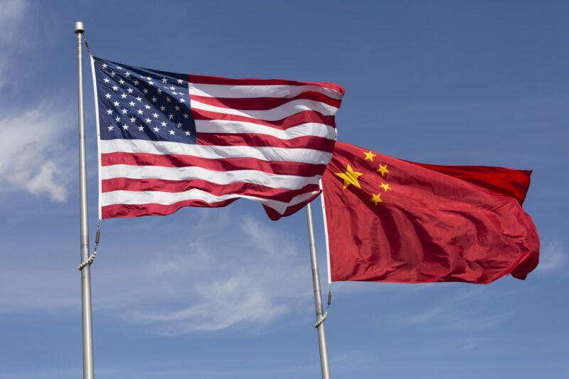 The flags of the United States and China fluttering from flagpoles on a windy day.