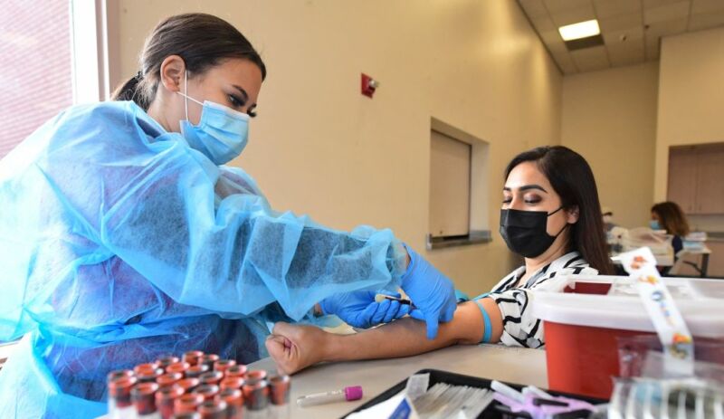 Image of a woman taking a blood sample from a seated person.