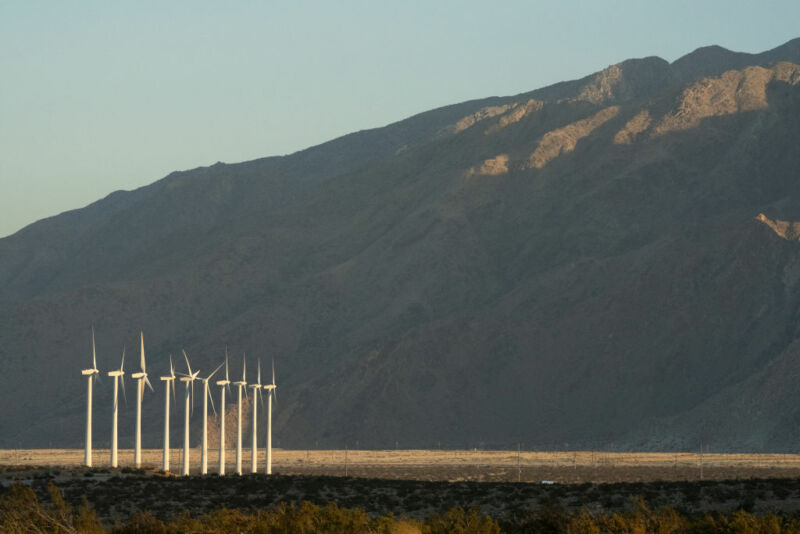 A wide angle shot of wind turbines at the foot of a mountain.