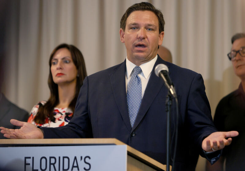 A man in a suit gestures while speaking at a podium