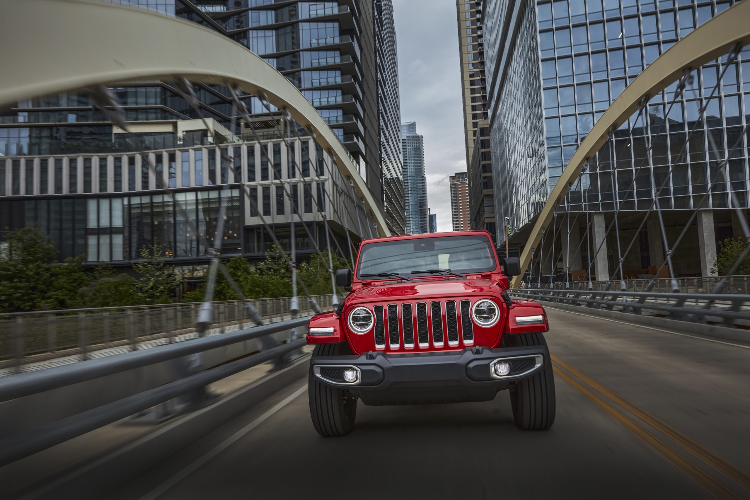 A red 2021 Jeep Wrangler Sahara 4xe crosses a bridge in Austin