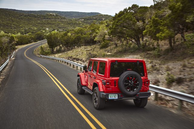 A red 2021 Jeep Wrangler Sahara 4xe drives away from the camera on a twisty road