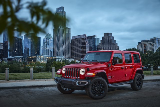 A red A red 2021 Jeep Wrangler Sahara 4xe parked with the Austin skyline in the background