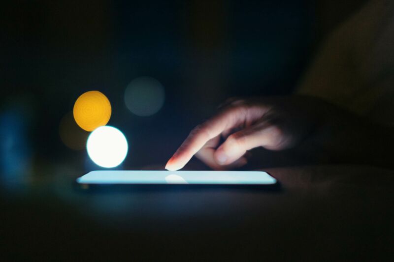 Gros plan sur un doigt féminin défilant sur l'écran du smartphone dans un environnement sombre.