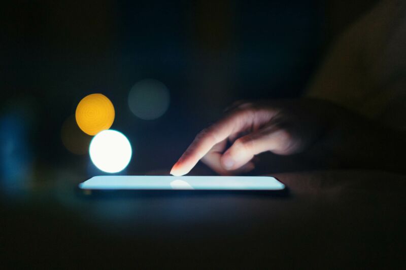 Close up of female finger scrolling on smartphone screen in dark environment.