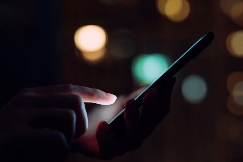 Closeup of woman's hand using a smartphone in the dark.