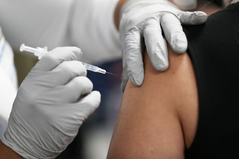Closeup of a person being getting a vaccination shot in the shoulder.
