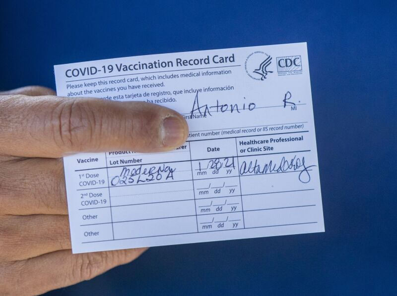 A man's hand holding a COVID vaccination card.