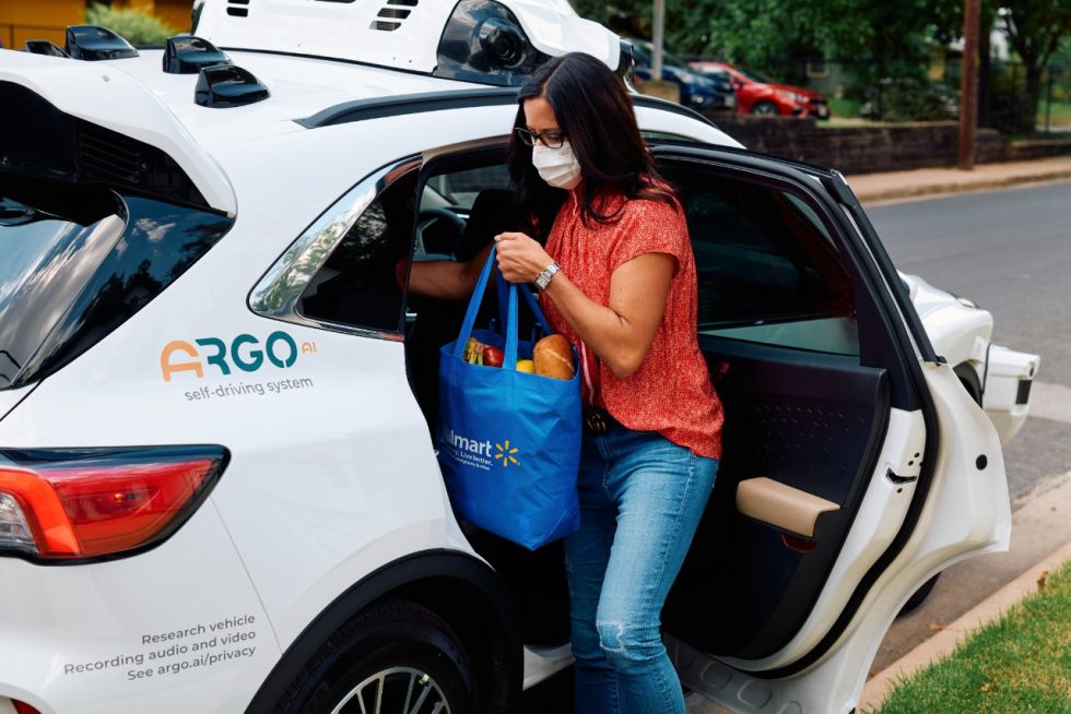 A human collects her Walmart delivery from an autonomous delivery vehicle operated by Ford and Argo AI.