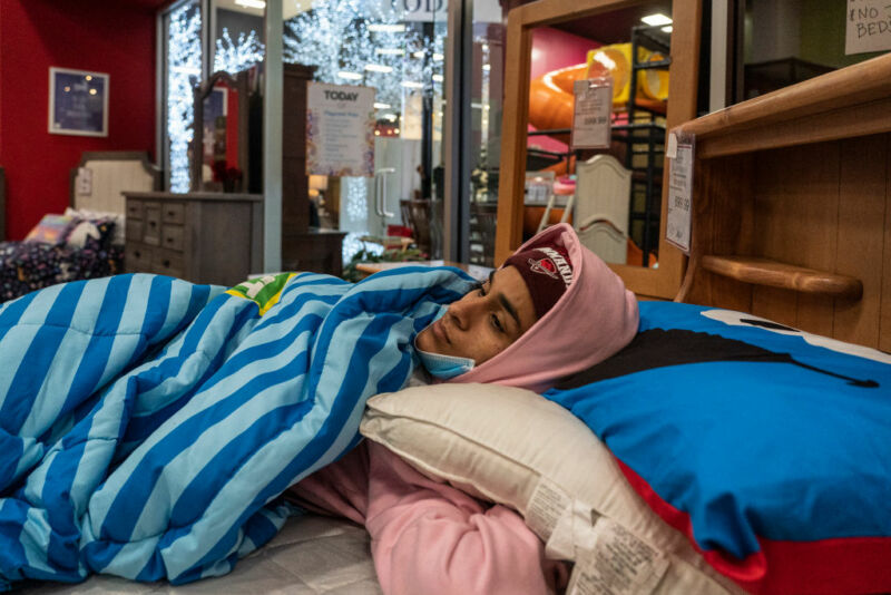 Image of a woman bundled against the cold on a bed in a furniture store.