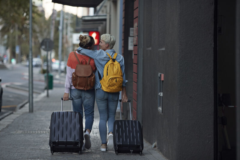 Two women pull suitcases as they walk down a sidewalk.