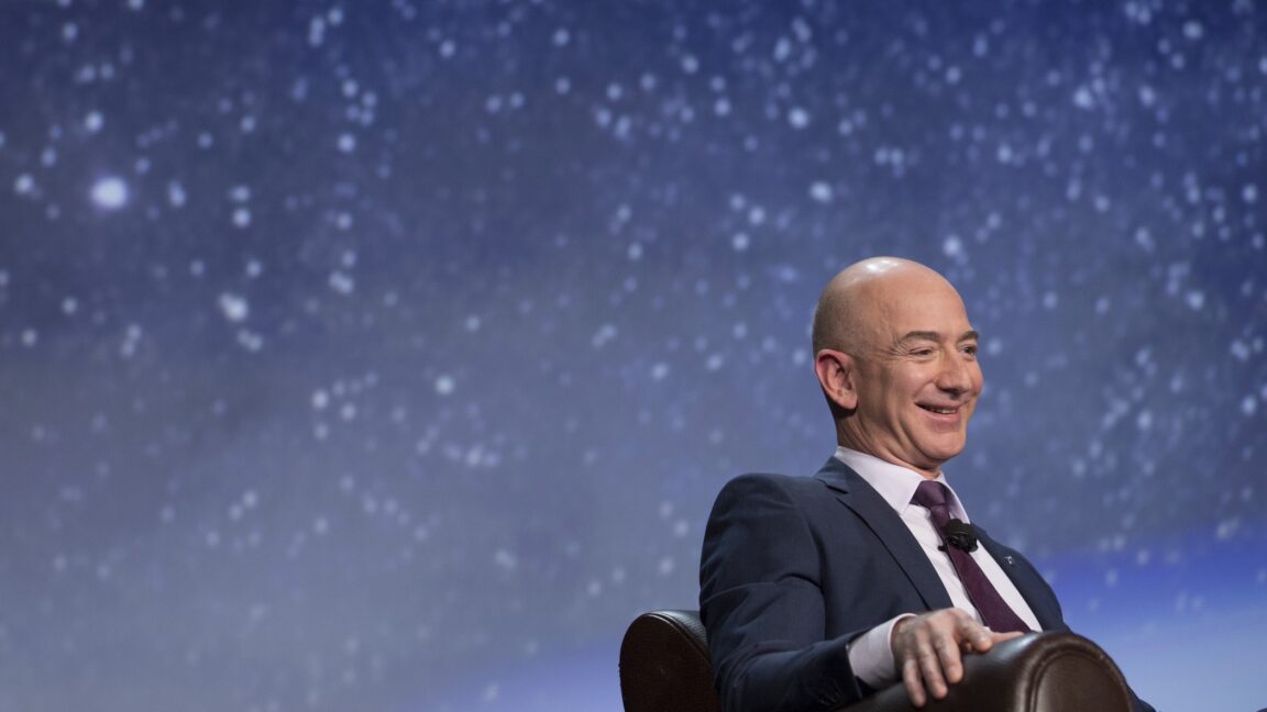 Jeff Bezos at a space conference, sitting in front of a picture of the stars in the night sky.