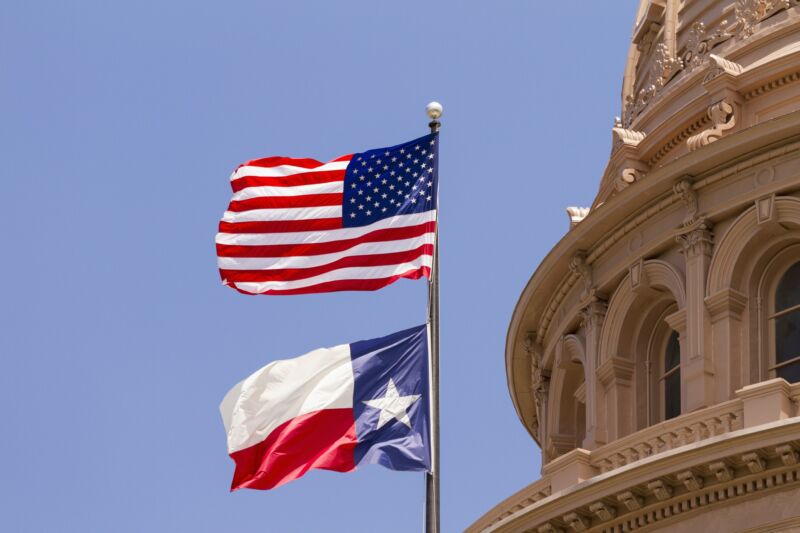 US and Texas flags seen in daytime outside the Texas State Capitol Building.