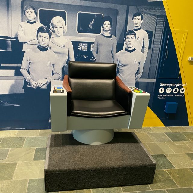 Exhibit visitors can take photographs while sitting in a reproduction of the captain's chair