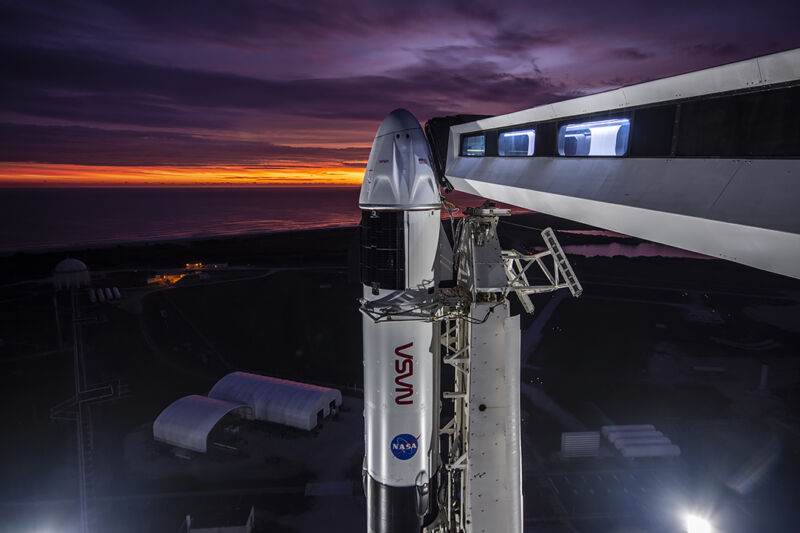 A rocket sits on a launch pad during a dawn streaked with purple and gold.