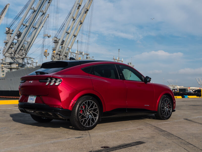 A red Ford Mustang Mach-E GT next to some navy ships