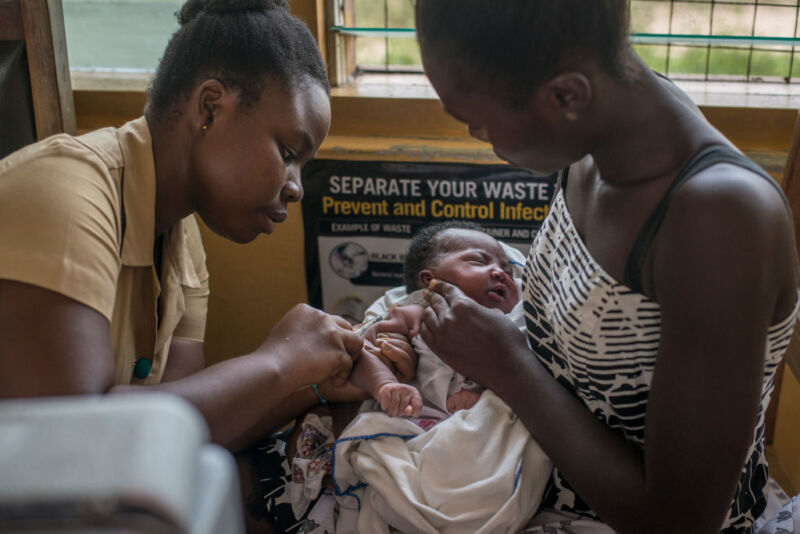 A woman holds a baby as it gets a vaccine.