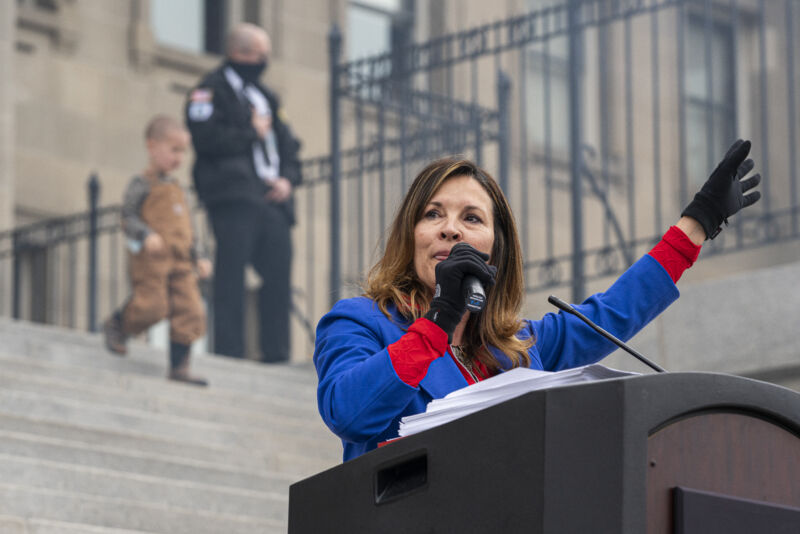 A warmly dressed woman speaks into a microphone.