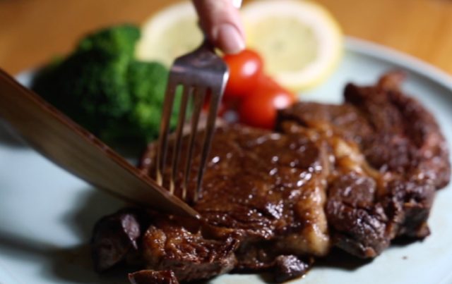 A UMD researcher cuts into a medium-well-done steak with a hardened wood knife.