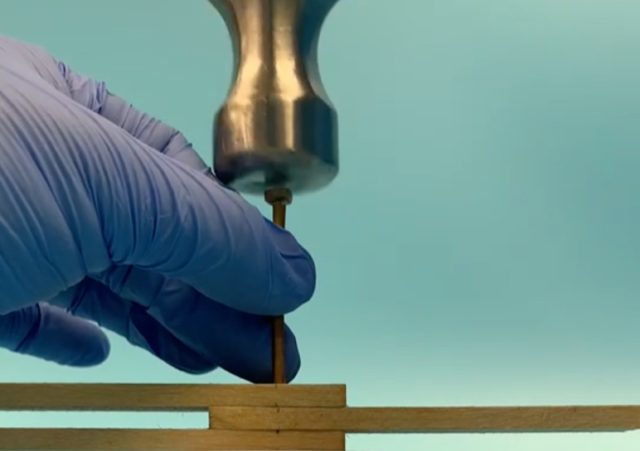 A UMD researcher tests a hardened wood nail by hammering it through three layers of wood boards.