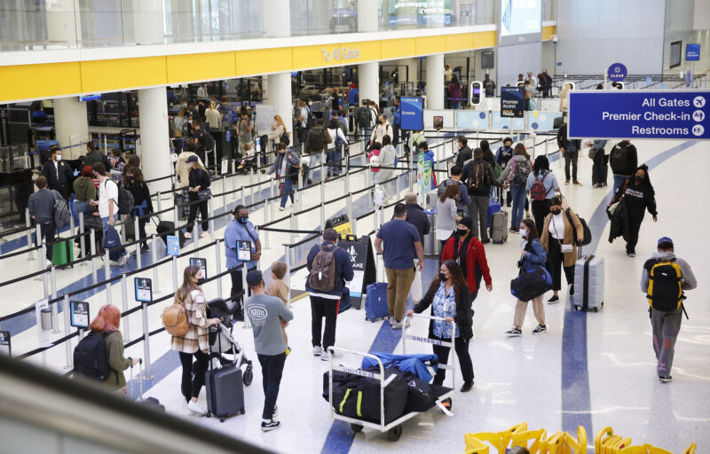 Masked travelers move through crowded airport.