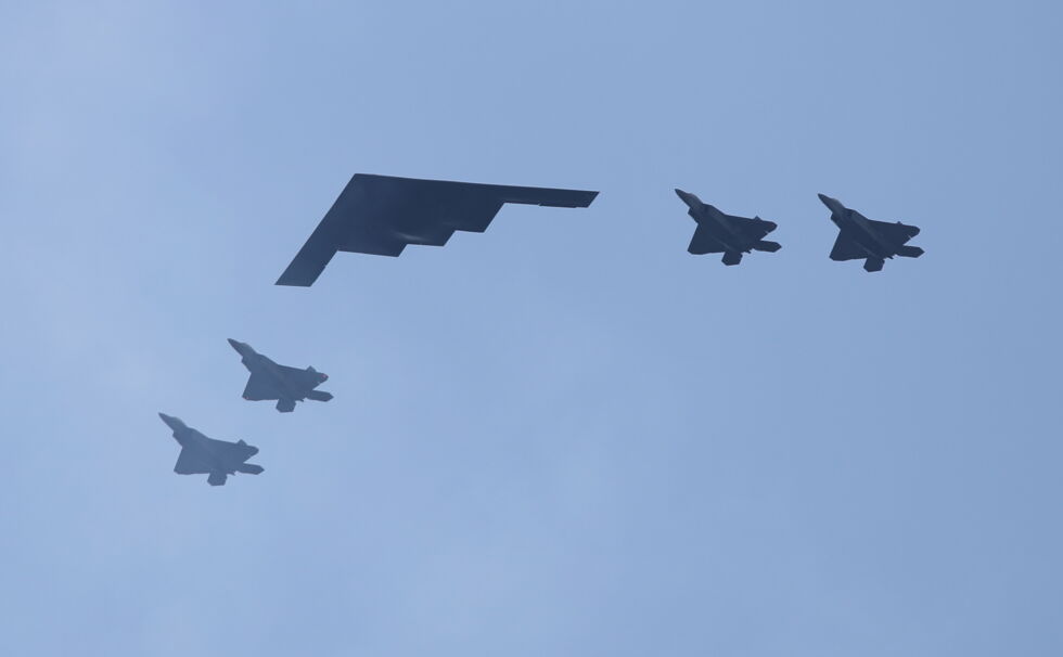 A B-2 stealth bomber, trailed by four F-22s. The B-2's sawtooth tail helps lessen its radar cross-section. Under the JADC2 doctrine, these planes can do all sorts of wild electronic things together.