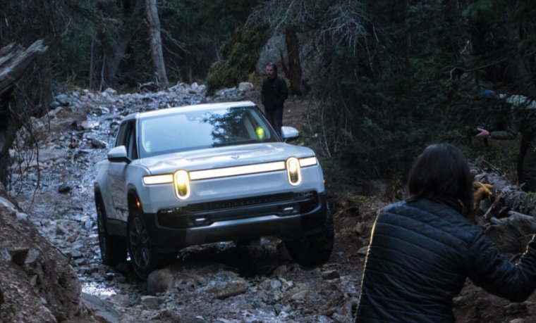 A white Rivian R1T truck drives up a trail