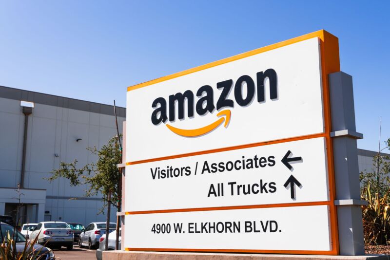 A sign outside an Amazon warehouse displays arrows and instructs visitors and associates to go in one direction and trucks to go in another direction.