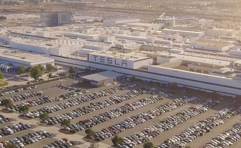 Aerial view of a Tesla factory with a large parking lot filled with cars.