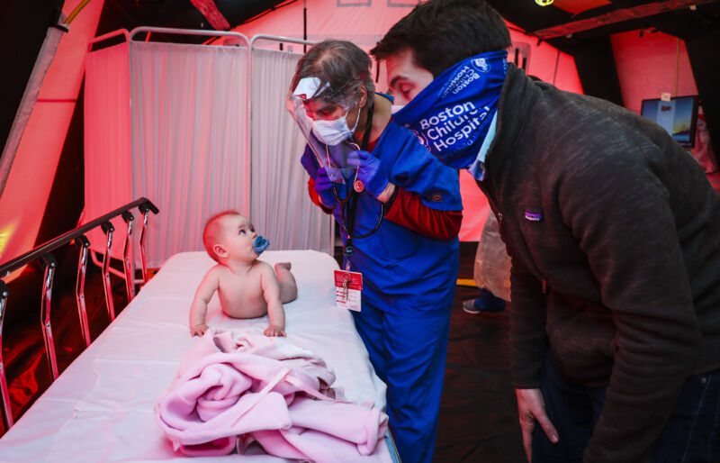 A Boston Medical Center pediatrician performs a checkup on an 8-month-old while her father provides her comfort in a pediatrics tent set up outside of Boston Medical Center in Boston on April 29, 2020. 
