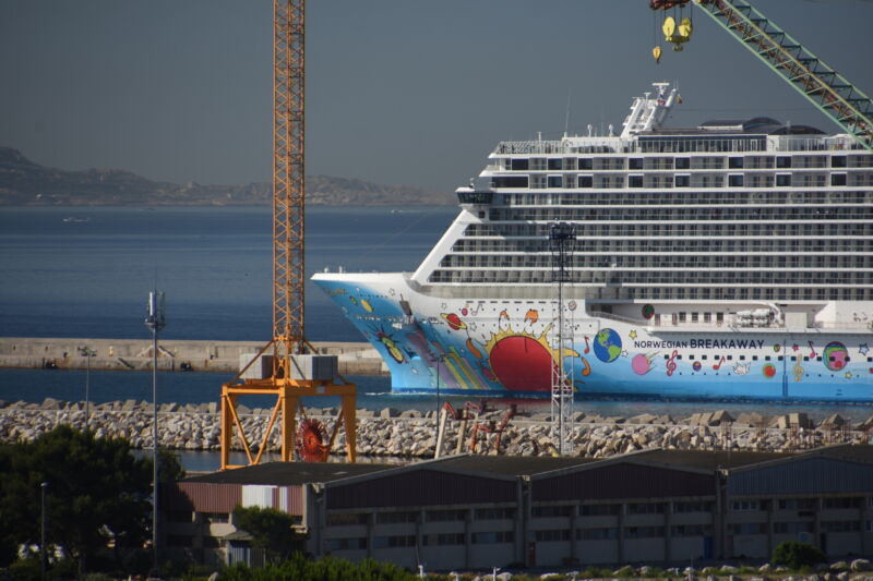 A cheerfully painted cruise ship towers over a rocky port.