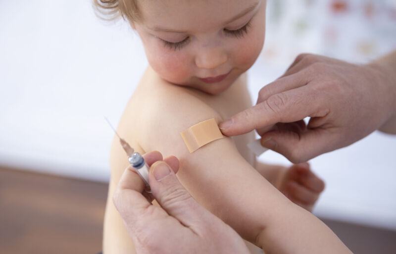 A small person looks at the band-aid being applied to their arm.