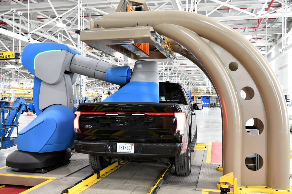 A big, friendly-looking robot does something to the load bed of a Ford F-150 Lightning.